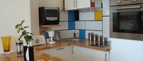 Une cuisine moderne avec des meubles blancs, un plan de travail en bois, une machine à café, un grille-pain, un évier et un four.