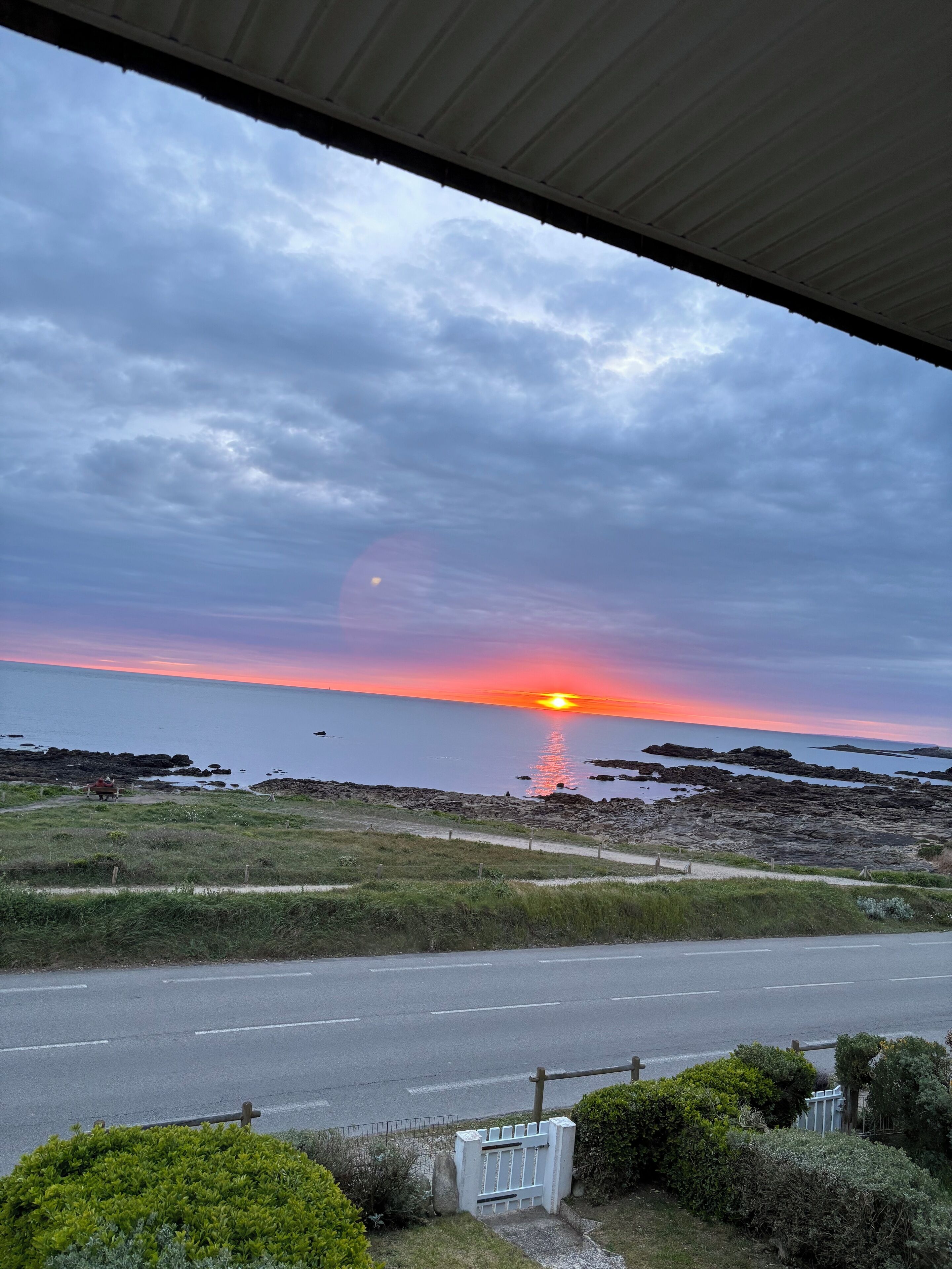 A sunset over a rocky coastline with a road in the foreground.