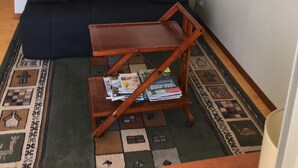 Ein Wohnzimmer mit einer schwarzen Couch, einem Holztisch mit Zeitschriften, einem dekorativen Spiegel und einem gemusterten Teppich.