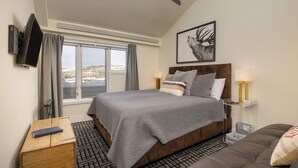 Habitación de hotel con cama, escritorio, silla, televisor y ventana con vistas a un paisaje nevado.