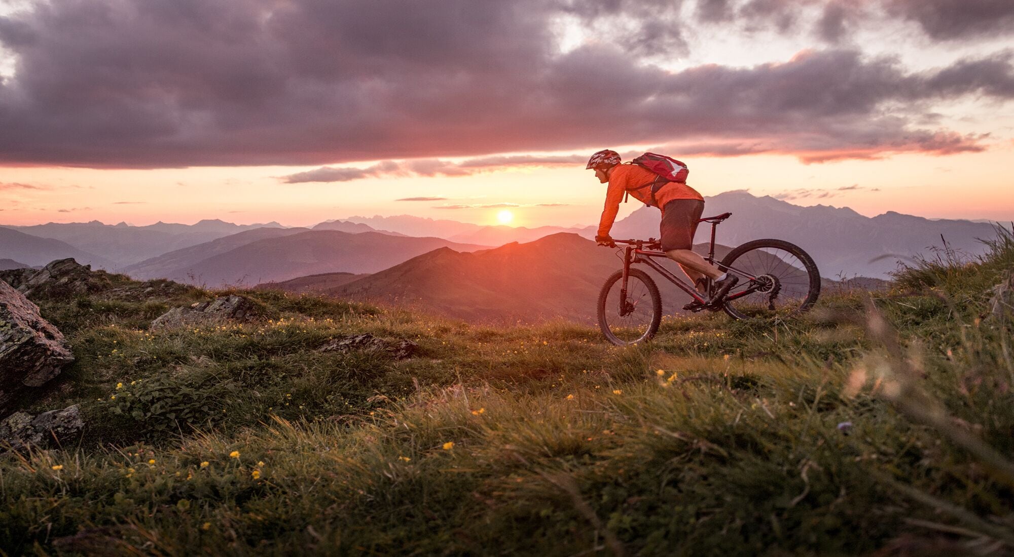 A mountain biker on a trail with a sunset in the background.