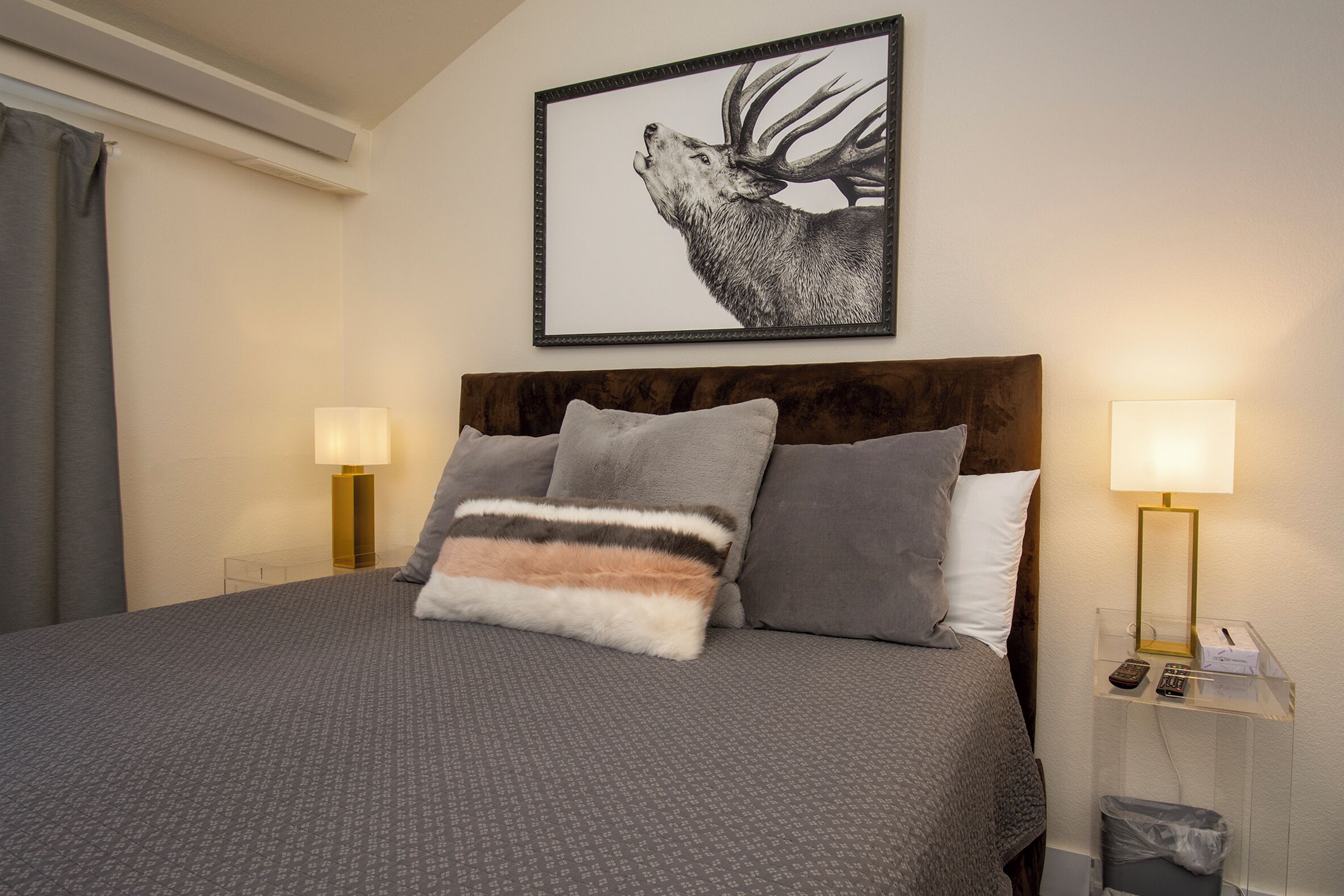 A neatly made bed with a grey patterned bedspread, two pillows, and a framed wildlife photograph above it.