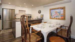Cocina moderna con armarios blancos, un refrigerador de acero inoxidable, sillas de madera y una mesa de comedor para cuatro.