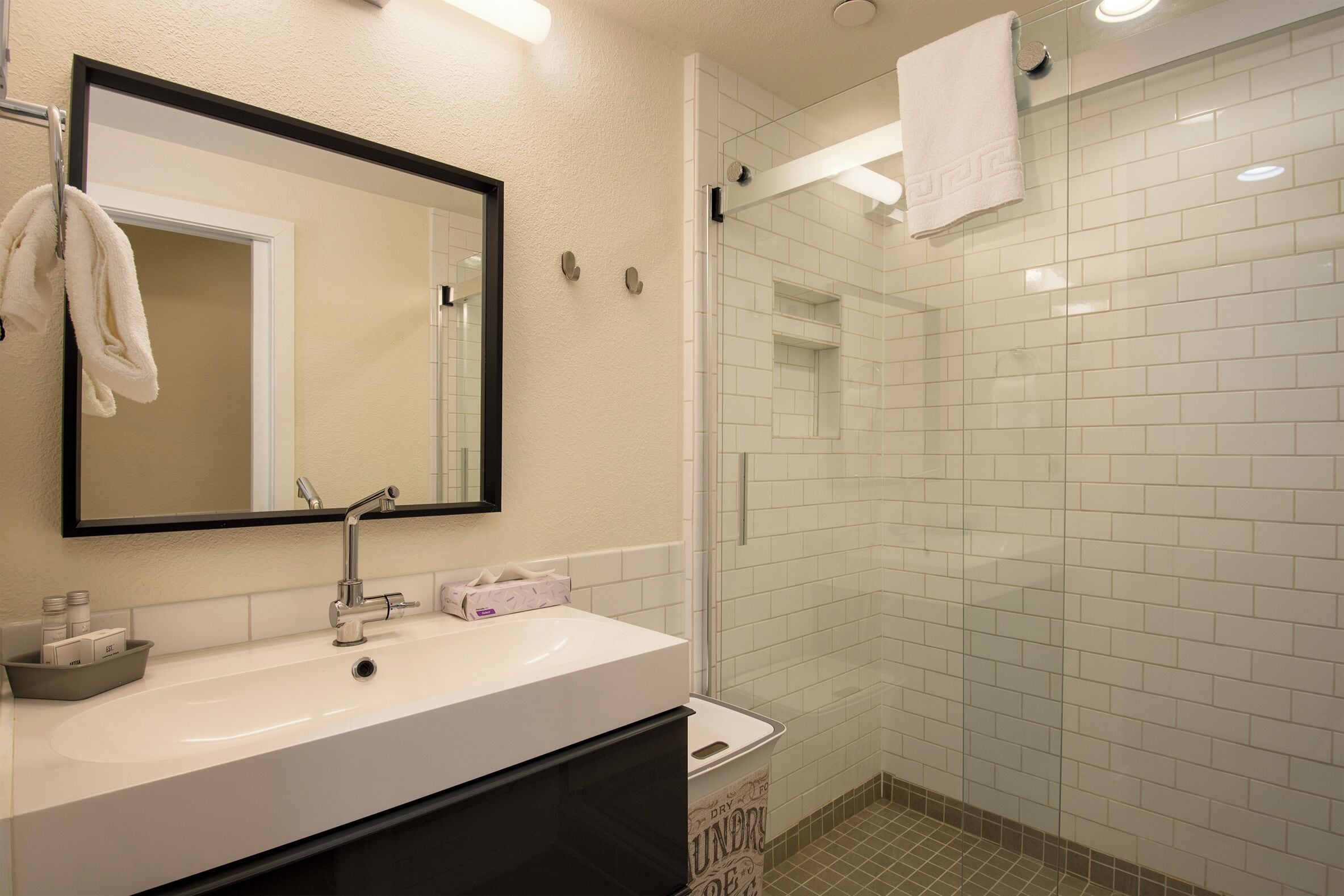 Une salle de bain moderne avec un lavabo blanc, un miroir et une douche carrelée.