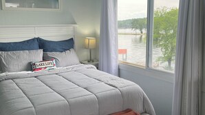 Una camera da letto con un letto, un comodino, una lampada, una ventola a soffitto e una finestra vista lago.