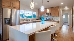 A modern kitchen with stainless steel appliances, a large island with bar stools, wooden cabinets, and pendant lighting. - The Perfect large Family Beach Getaway! 3 Min Walk To Beach - Family reunions! (Encinitas)