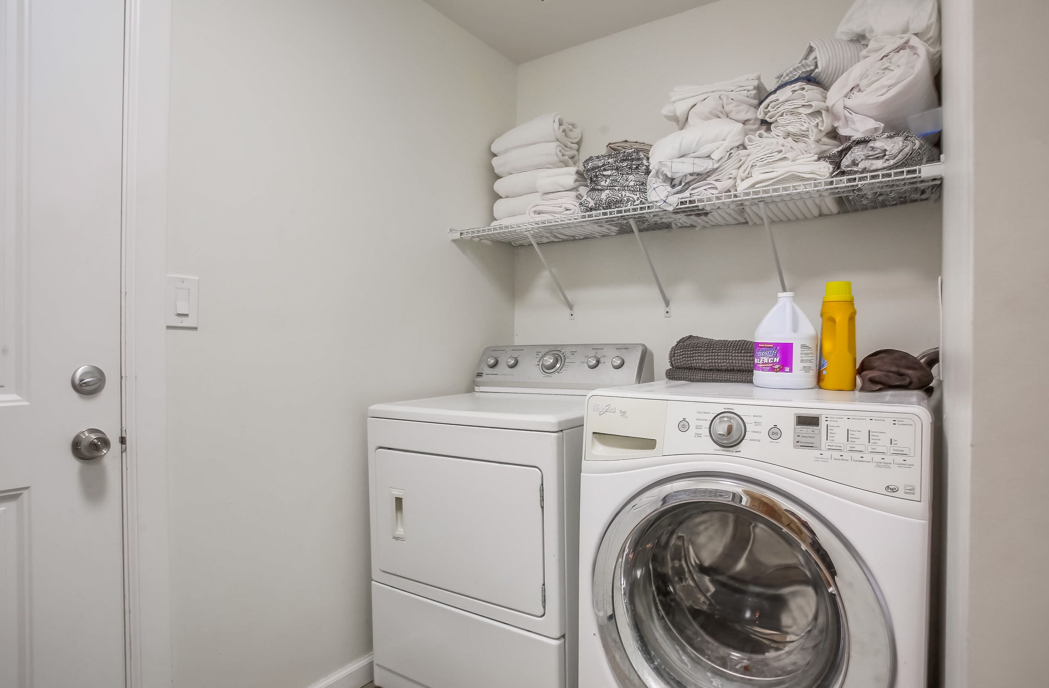 Un espace buanderie comprenant un lave-linge, un sèche-linge et une étagère avec des serviettes pliées.