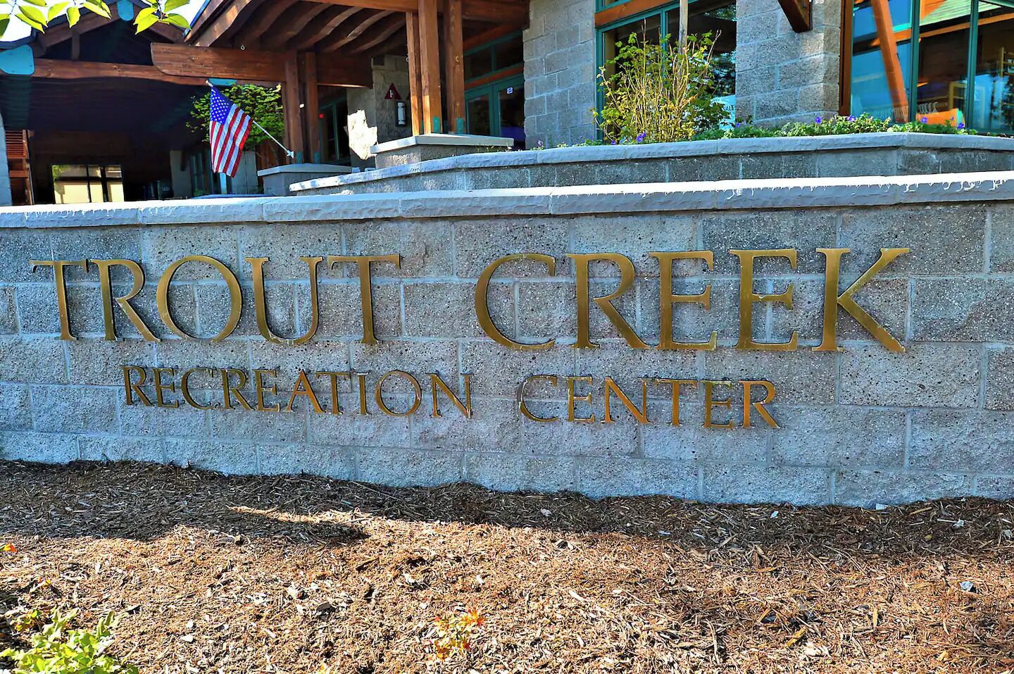 A sign for Trout Creek Recreation Center with a stone wall and an American flag.