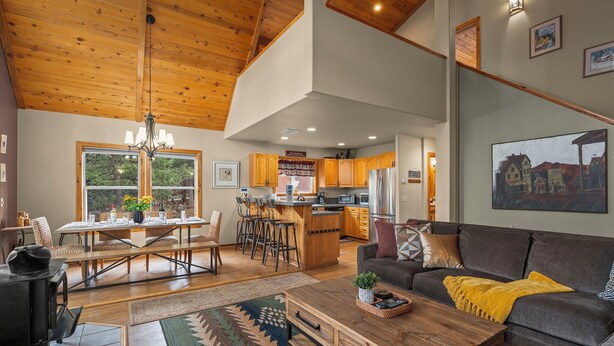 A spacious living room with a wooden ceiling, a dining area, kitchen, and a cozy seating area.