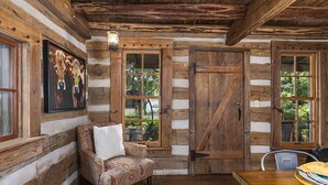 Interior de una cabaña de troncos con un sofá, una mesa de comedor y un cuadro de vacas.