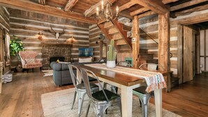 Interior rústico de una cabaña de troncos con comedor, sofá y chimenea de piedra.