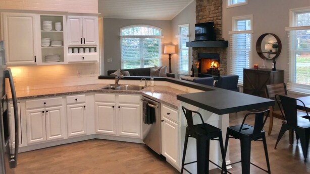 A modern kitchen with white cabinets, a stone fireplace, and a dining area with bar stools. - Douglas Beach Rental - Close to everything! Sleeps up to 12.  (Douglas)