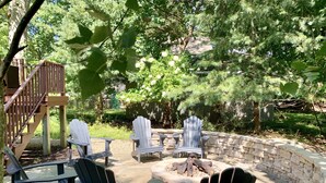 A patio area with Adirondack chairs, a stone fire pit, and a wooden deck. - Douglas Beach Rental - Close to everything! Sleeps up to 12.  (Douglas)
