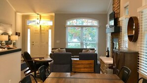 A dining area with a wooden table and chairs, a built-in bench with cushions, a stone fireplace, and a large window with a view of trees. - Douglas Beach Rental - Close to everything! Sleeps up to 12.  (Douglas)
