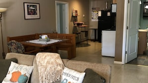 A living room with a couch, a dining table, and a kitchen area in the background. - The Bunkhouse  318 E. Main St. Warsaw, Mo. (Warsaw)