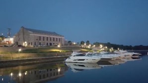 A marina with several yachts docked, a large building with lights on its roof, and a calm body of water reflecting the scene. - The Bunkhouse  318 E. Main St. Warsaw, Mo. (Warsaw)