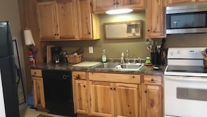A kitchen with wooden cabinets, a dishwasher, a stove, and a sink. - The Bunkhouse  318 E. Main St. Warsaw, Mo. (Warsaw)