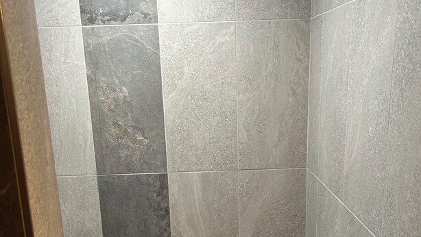 Un espace douche avec un mur et un sol carrelés, un banc et un aménagement d’angle.