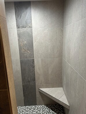 A shower area with a tiled wall and floor, a bench, and a corner design.