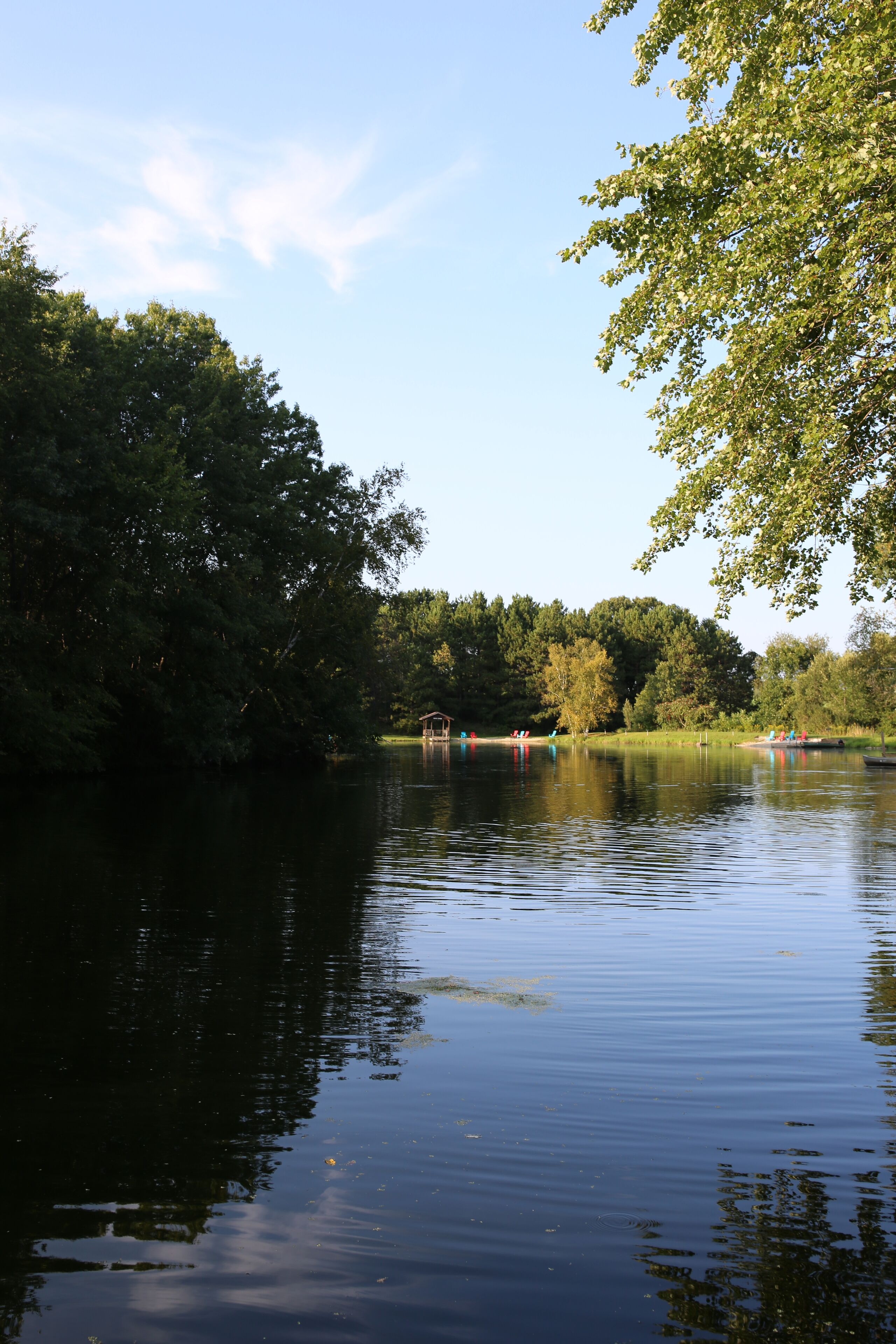 A calm river with trees on both sides and a small bridge in the distance.
