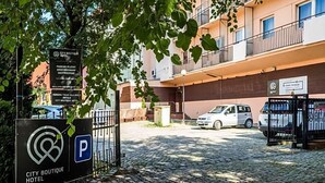 UN HÔTEL-BOUTIQUE URBAIN doté d’un parking, avec une voiture blanche garée devant et un bâtiment avec des balcons en arrière-plan.