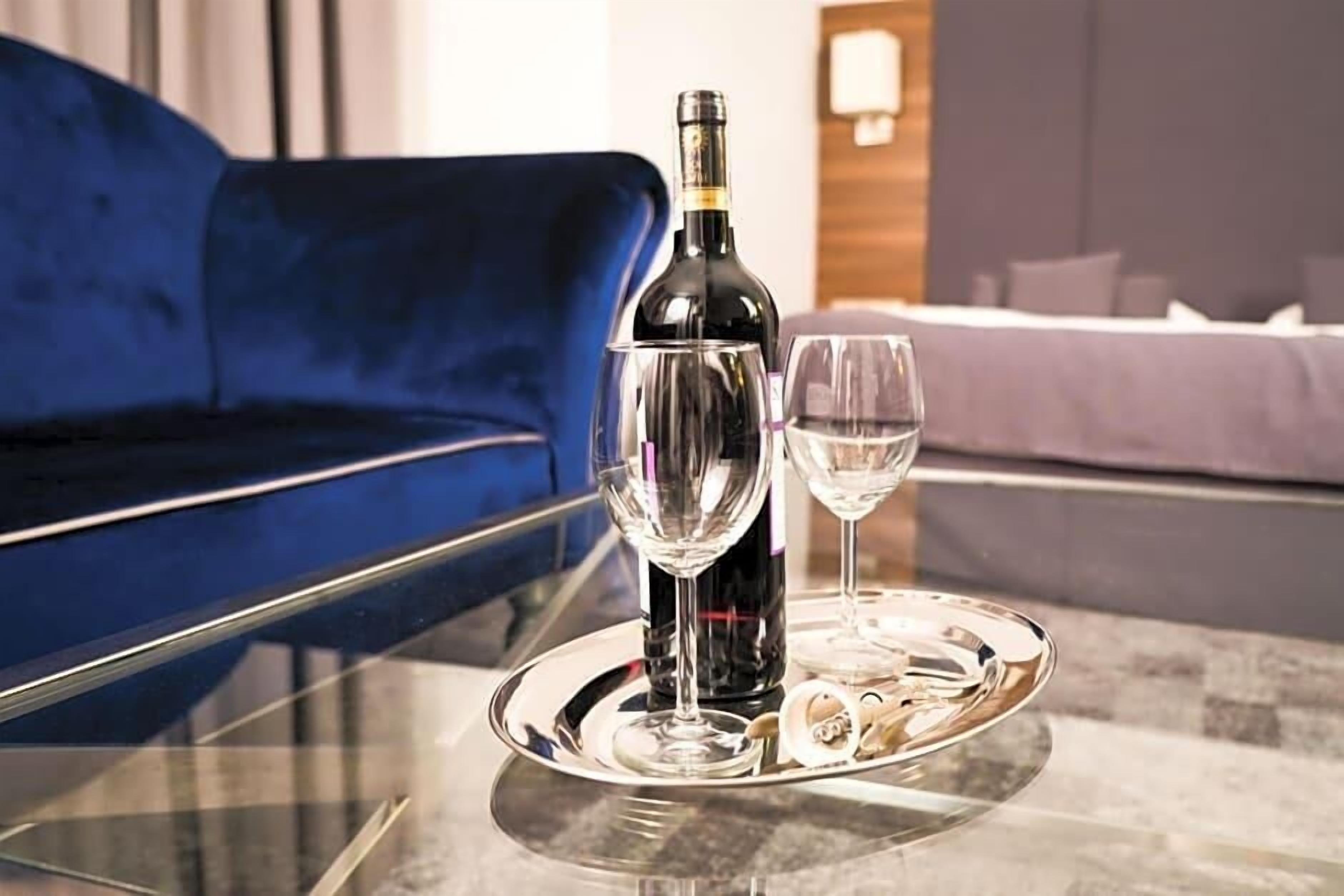 En flaska vin, två glas och ett bricka på ett glasbord i ett hotellrum.
