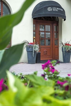 A hotel entrance with a brown door, a black awning, and potted plants.
