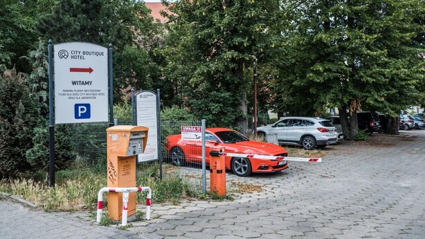 Un espace de stationnement avec un panneau indiquant « City Boutique Hotel Witamy », une voiture rouge et un parcmètre.