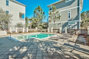 A backyard with a swimming pool, a patio with lounge chairs, and a wooden fence.