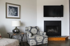 A living room with a fireplace, a sofa, a chair, a lamp, and a framed picture on the wall. - Dewey Beach Oceanfront (Dewey Beach)