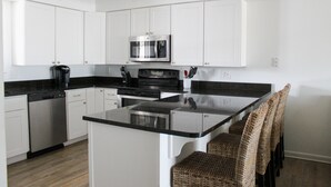 Una cocina moderna con armarios blancos, un microondas de acero inoxidable, encimeras negras y sillas de mimbre.