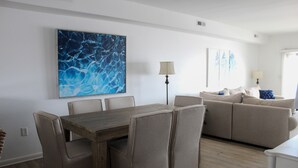 Una sala de estar moderna con una mesa de comedor, sofás color beige y un cuadro abstracto grande en la pared.