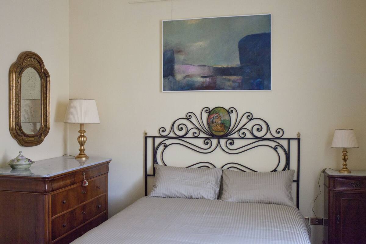 Une chambre à coucher avec un lit, une commode, un miroir et un tableau accroché au mur.