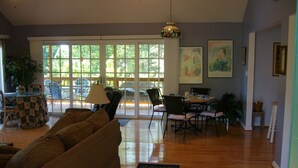 A spacious living room with a large window, a sofa, a dining table, and chairs. - 4/3, Waterfront Home w/ Covered Dock, Child Sand Play Pit,  Pet Friendly! (Seneca)