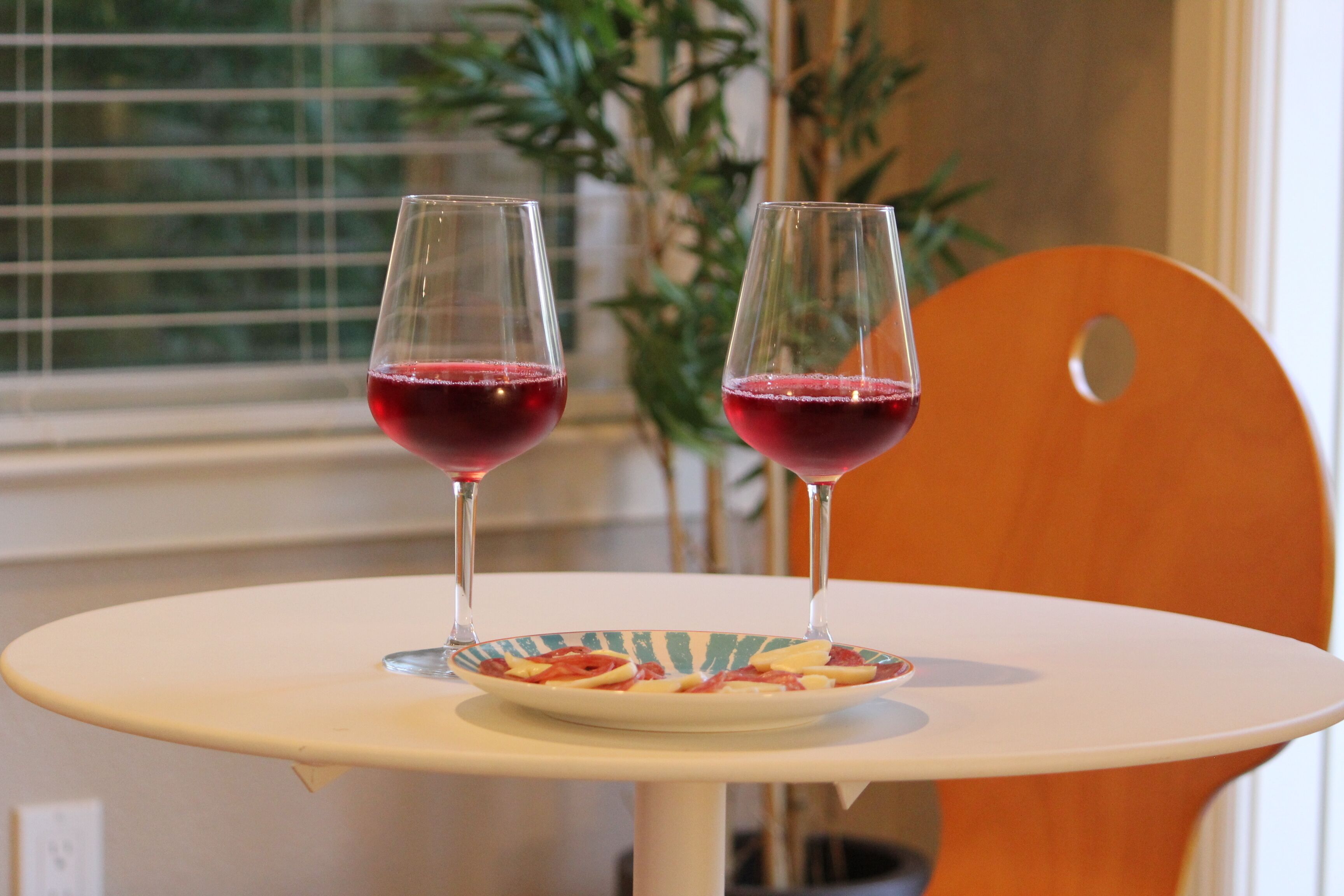 Deux verres à vin sont posés sur une table, à côté d’une assiette de nourriture.