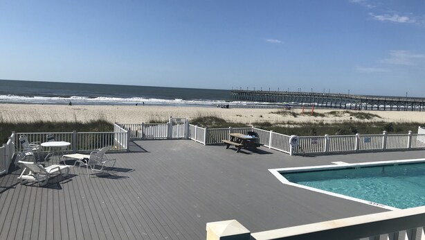 A deck with lounge chairs and a pool, overlooking a beach and pier. - REDUCED OFF-SEASON RATES!  Oceanfront Condo, Sleeps 4, Close to Everything! (Ocean Isle Beach)