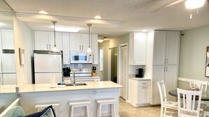 A modern kitchen with white cabinets, a central island, and pendant lighting. - REDUCED OFF-SEASON RATES!  Oceanfront Condo, Sleeps 4, Close to Everything! (Ocean Isle Beach)