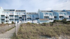 A beachfront hotel with multiple balconies, a sandy walkway, and a wooden fence. - REDUCED OFF-SEASON RATES!  Oceanfront Condo, Sleeps 4, Close to Everything! (Ocean Isle Beach)
