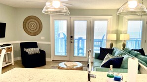 A modern living room with a kitchen area, featuring a large window, a ceiling fan, and a dining table. - REDUCED OFF-SEASON RATES!  Oceanfront Condo, Sleeps 4, Close to Everything! (Ocean Isle Beach)
