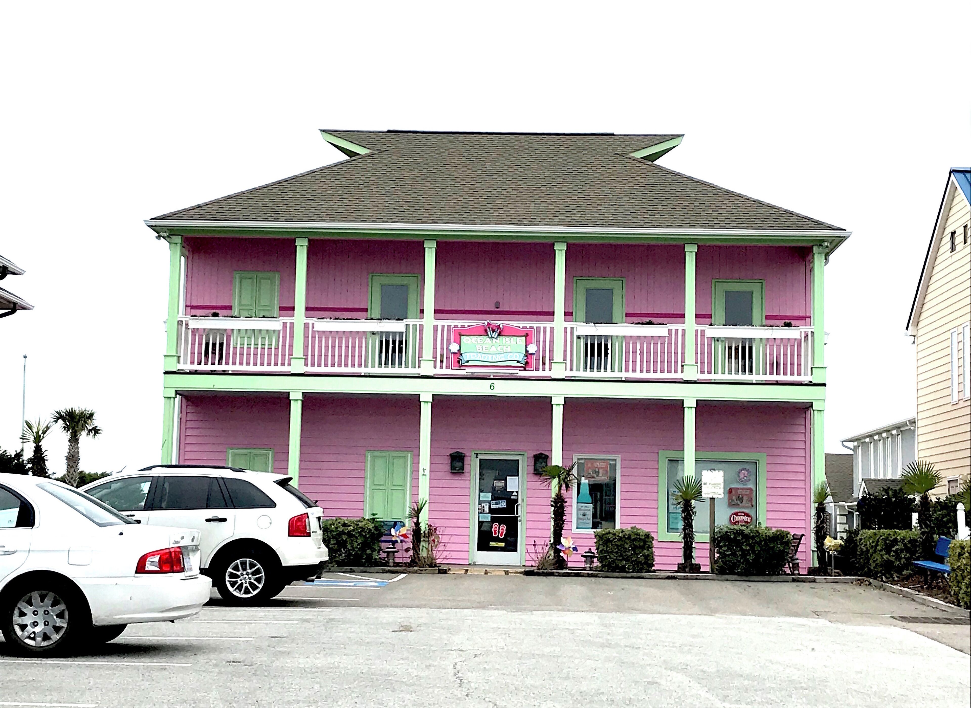 Un edificio de dos pisos con fachada rosa y detalles verdes, que muestra un letrero que dice 'Ocean Breeze'.