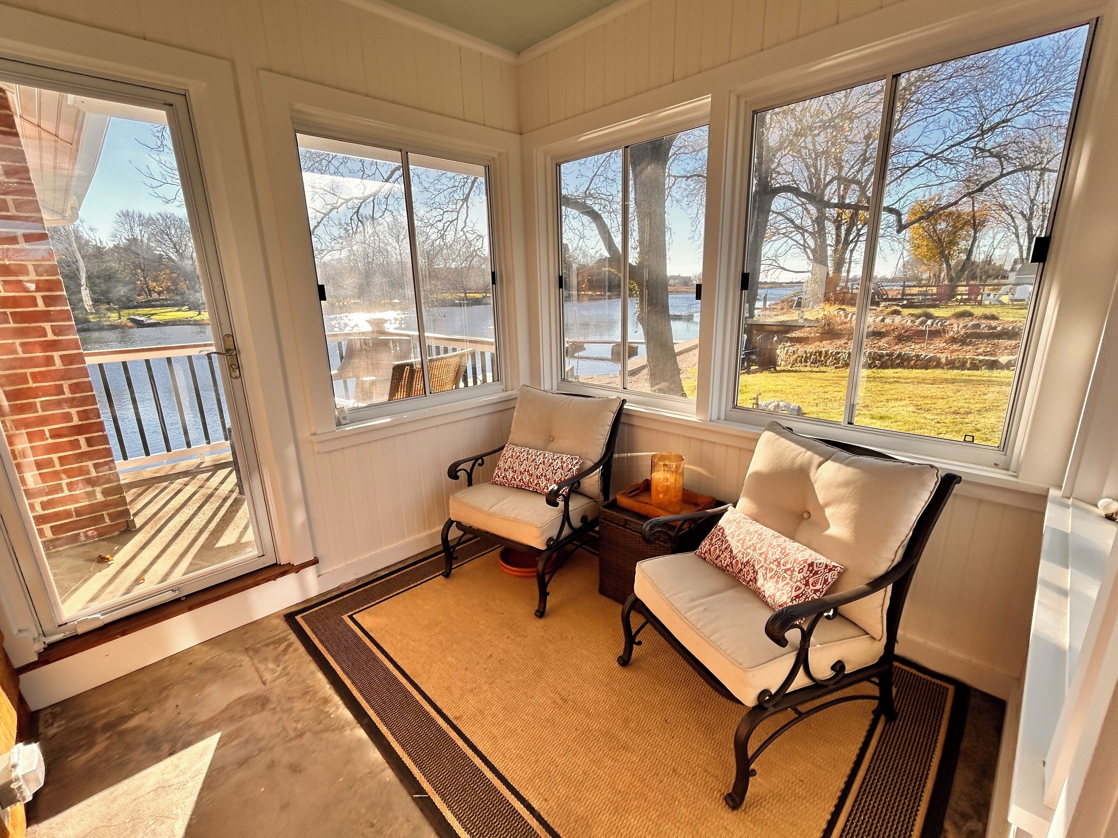 Une véranda avec deux fauteuils, une petite table et une vue sur un lac et des arbres.