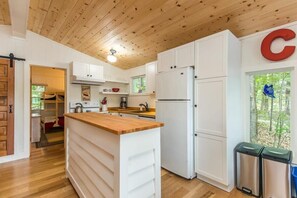 Moderni keittiö, jossa on valkoiset kaapit, puinen työtaso ja ruostumattomasta teräksestä valmistettu jääkaappi.