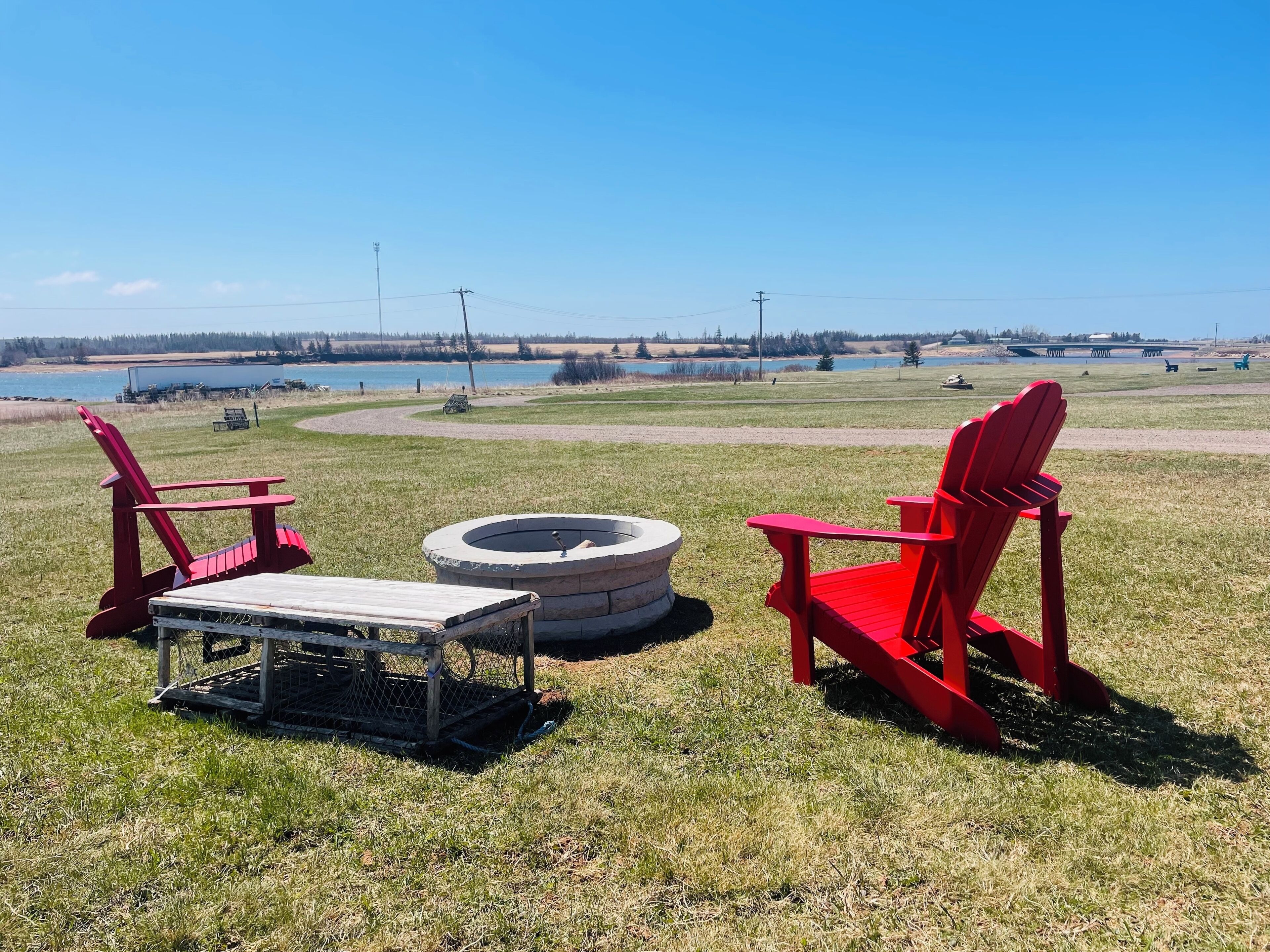 A grassy outdoor area with two red Adirondack chairs and a fire pit.