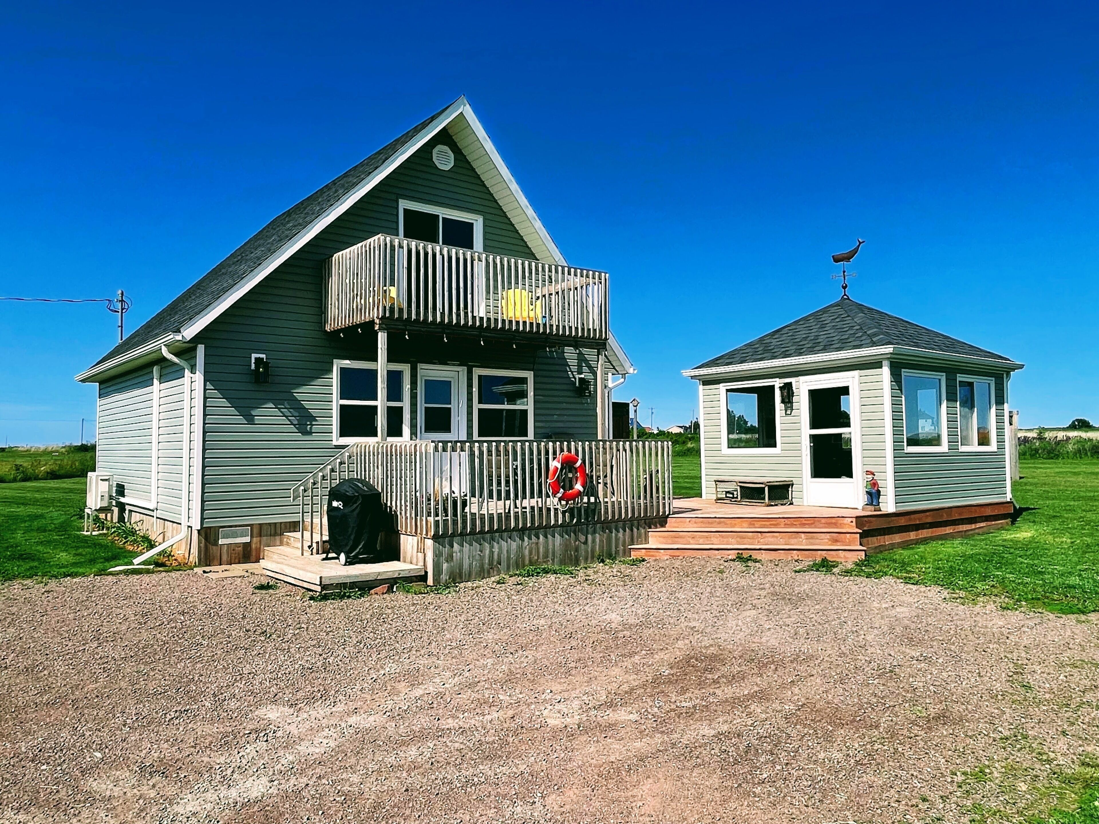 Une maison à deux étages avec un balcon, une petite dépendance attenante et une allée gravillonnée.