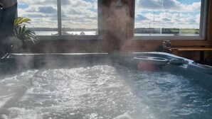 A hot tub with a view of a lake and sky through a window. - Rest Ashored in Anne's land!- Hot tub, Kayaks Centrally located, stunning views. (Kensington)
