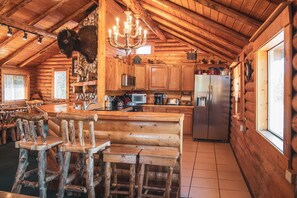 A rustic wooden cabin with a kitchen area featuring a refrigerator, microwave, and wooden bar seating. - Sportsman Cabin, 15 miles  to West Yellowstone ! Hot Tub, on Snowmobile Trail.   (Island Park)