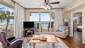 Una sala de estar con televisión, ventilador de techo, sofá, mesa de centro y vista a la playa.
