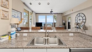 Una cocina con encimeras de granito, pileta de acero inoxidable y ventilador de techo.