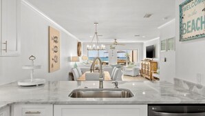 Een moderne keuken met een spoelbak, een eetgedeelte met een kroonluchter, en uitzicht op het strand door de ramen.