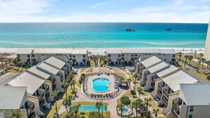 Een resort met een centraal zwembad, meerdere gebouwen en uitzicht op het strand.